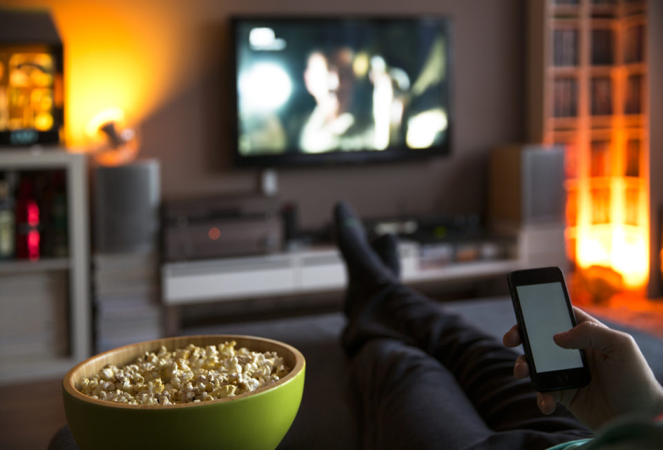 Man relaxing at home watching tv and eating popcorn and surfing internet