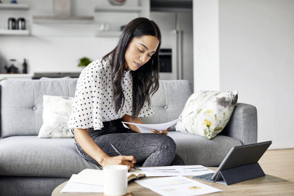 Young woman analyzing bills while writing in notebook.