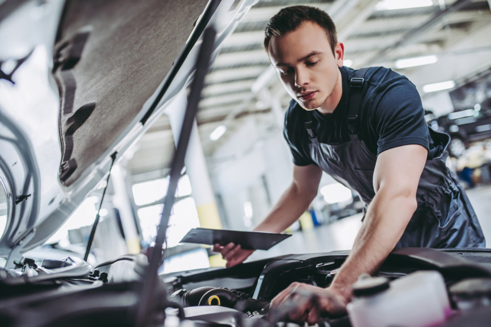mechanic in uniform is examining the car while working in auto service. Car repair and maintenance.