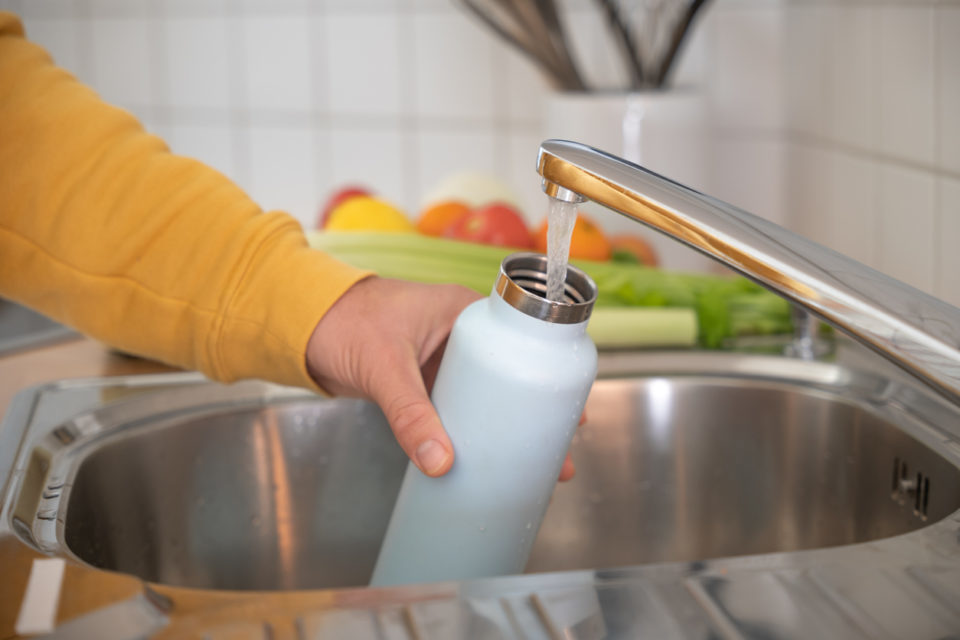 Man fills up reusable water bottle in the kitchen