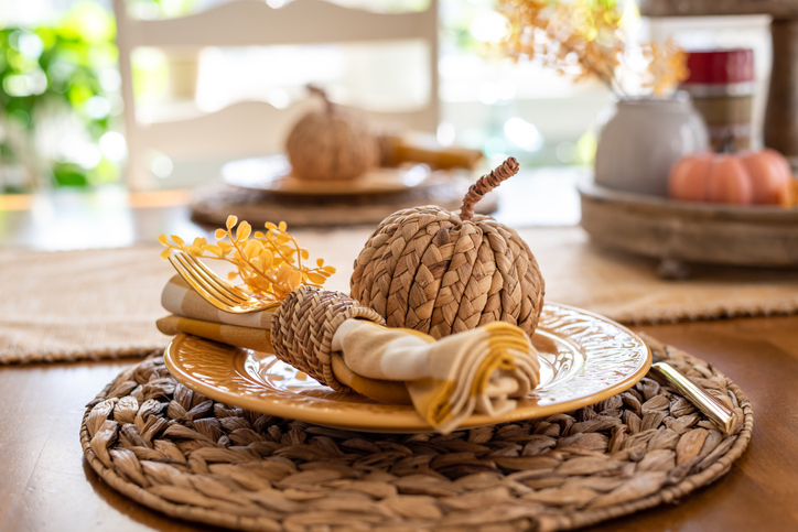 Stylish fall place setting in gold and white with wicker accents in light and bright dining room