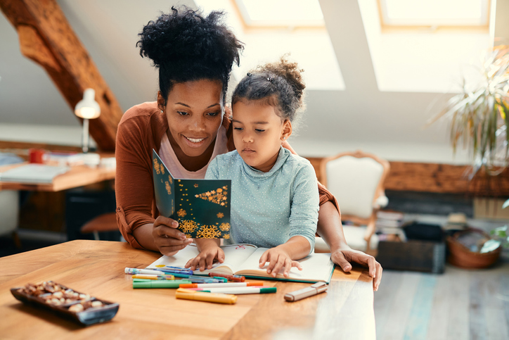 Happy African American mother and daughter reading Christmas card while drawing at home.