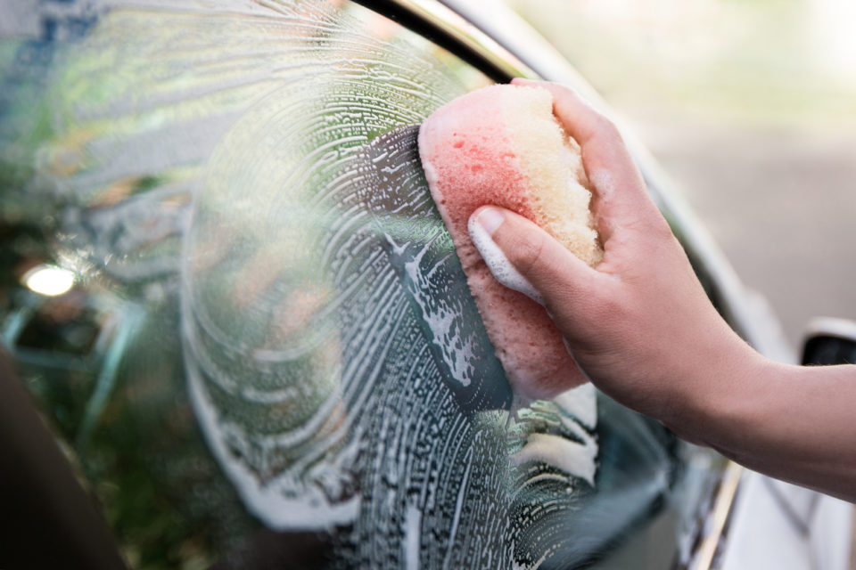 close up of male hand holding sponge and washing car window
