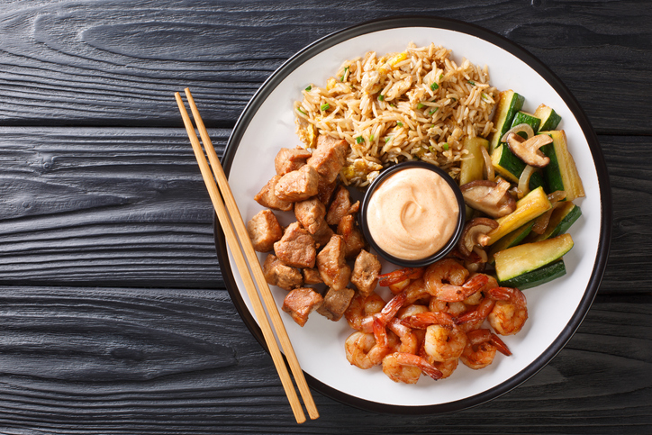 Serving hibachi of rice, shrimp, steak and vegetables served with sauce closeup in a plate on the table.