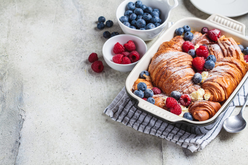 Croissant baked french toast with cream cheese and berries in a dark oven dish, copy space. Delicious breakfast recipe concept.