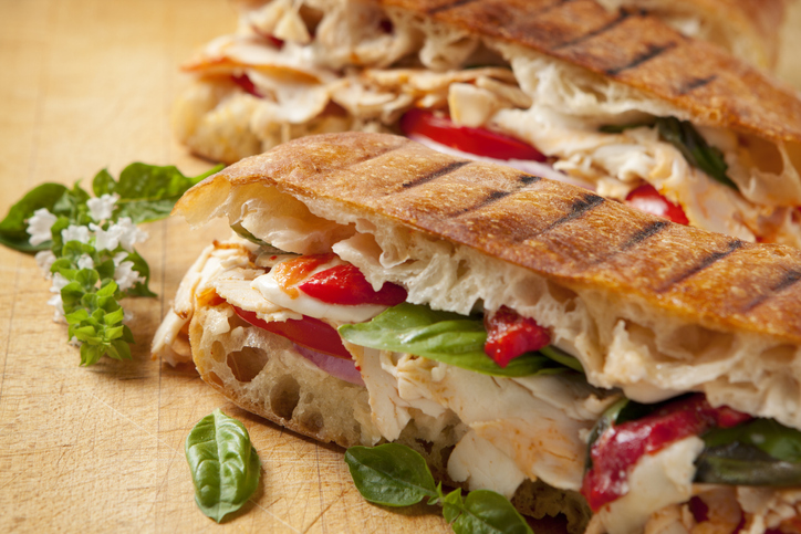 Freshly cooked panini sandwiches with chicken, basal, roasted red peppers, tomatoes, red onions, and mozzarella cheese served on ciabatta bread.
